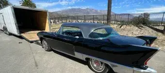 A black vintage car getting into an enclosed trailer