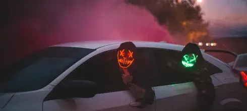 Men in glowing Halloween masks driving car at night