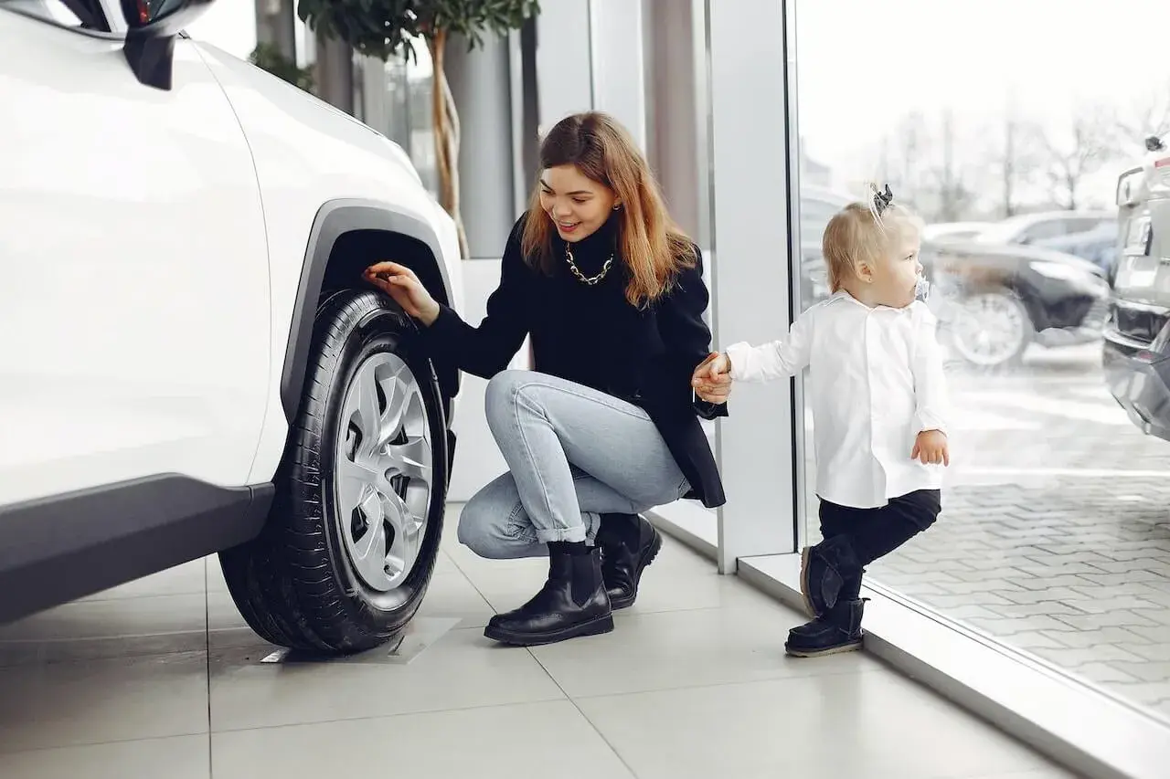 Happy woman with daughter checking car wheel in car showroom Happy woman with daughter checking car wheel in car showroom