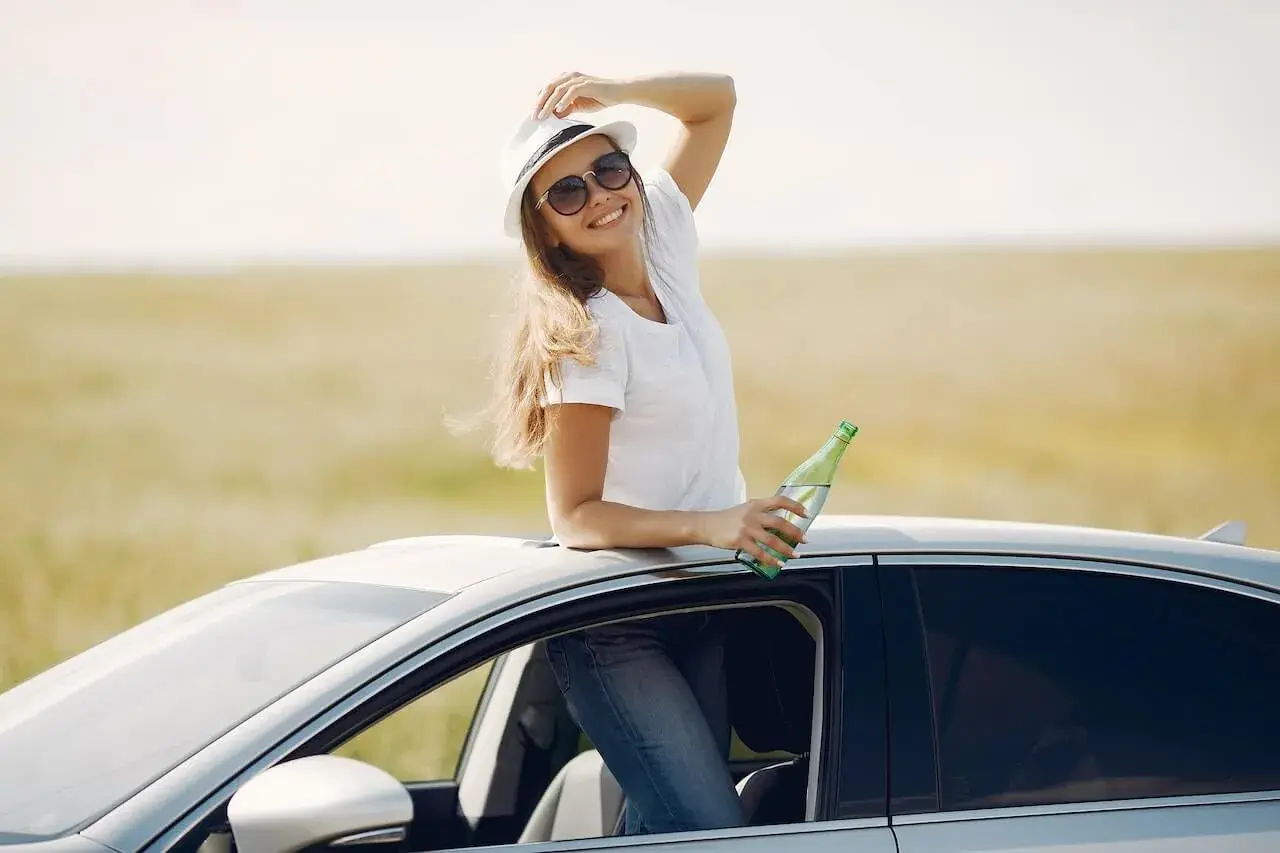 Cheerful young woman with refreshing drink in automobile during car trip Cheerful young woman with refreshing drink in automobile during car trip